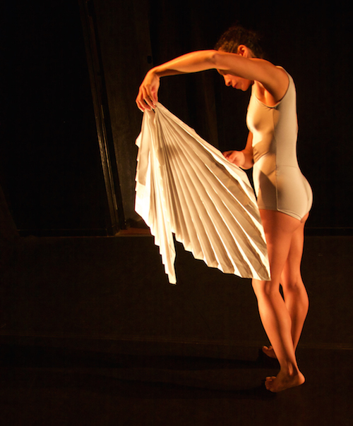 Dance Marielis Garcia clad in a light blue leotard holds out an intricately folded white paper sculpture that billows out from the bottom